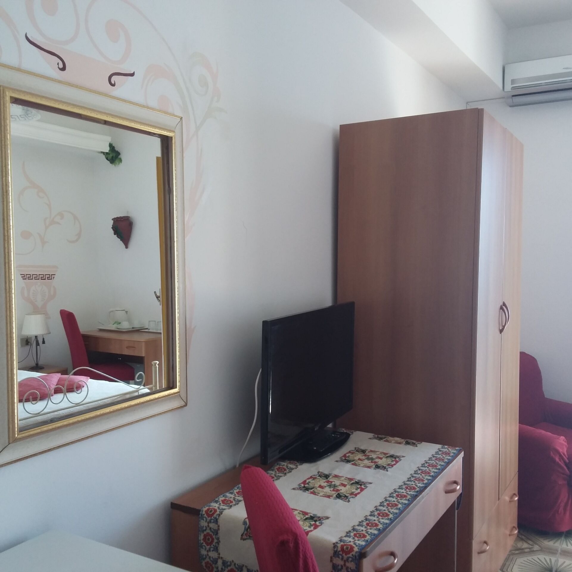Quarto com cama, escrivaninha com computador, guarda-roupa e espelho.