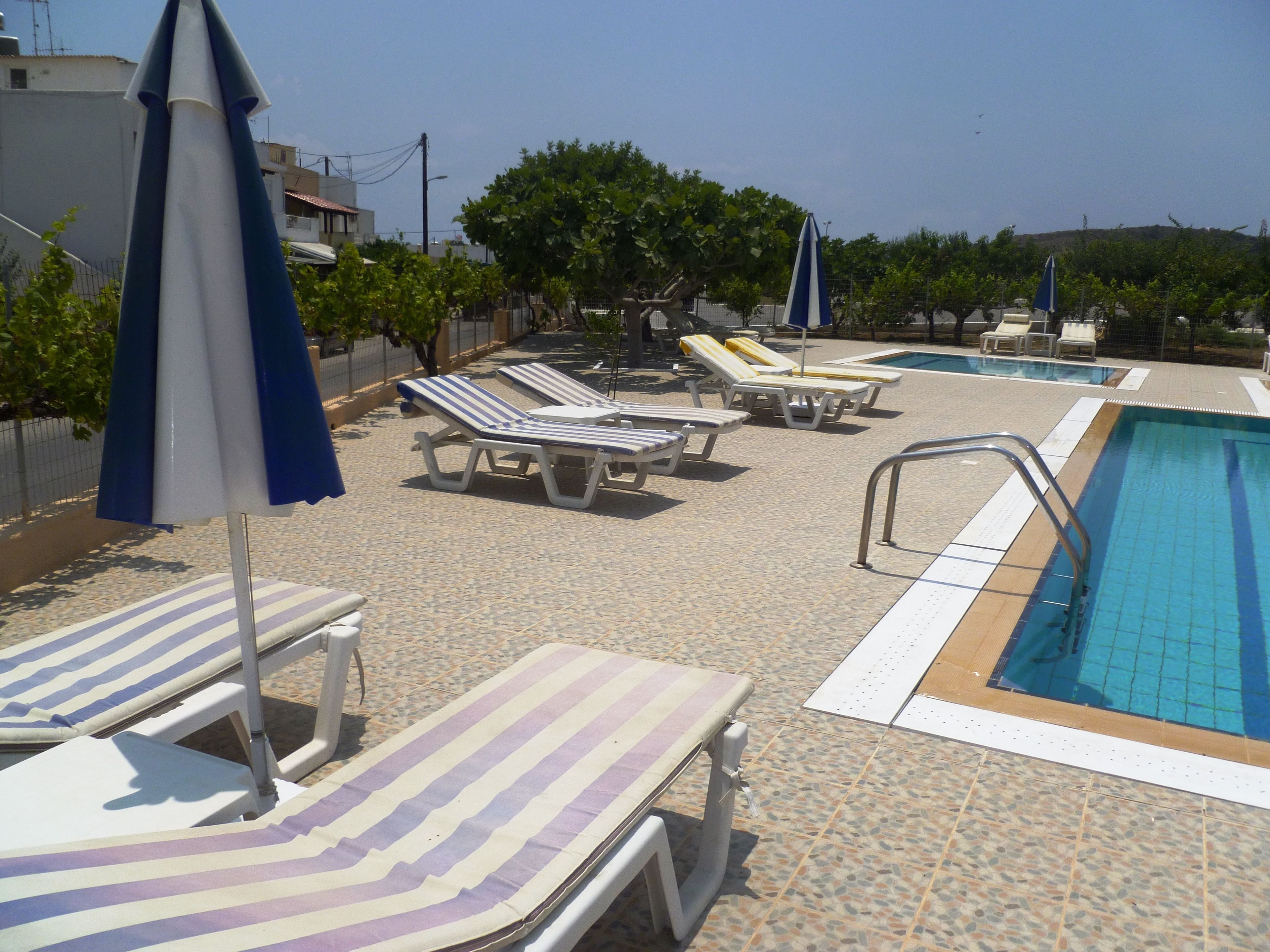 Area piscina con lettini e ombrelloni, una piscina e un solarium piastrellato.