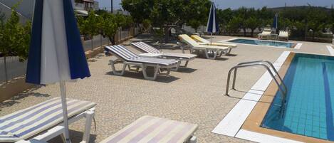 Area piscina con lettini e ombrelloni, una piscina e un solarium piastrellato.