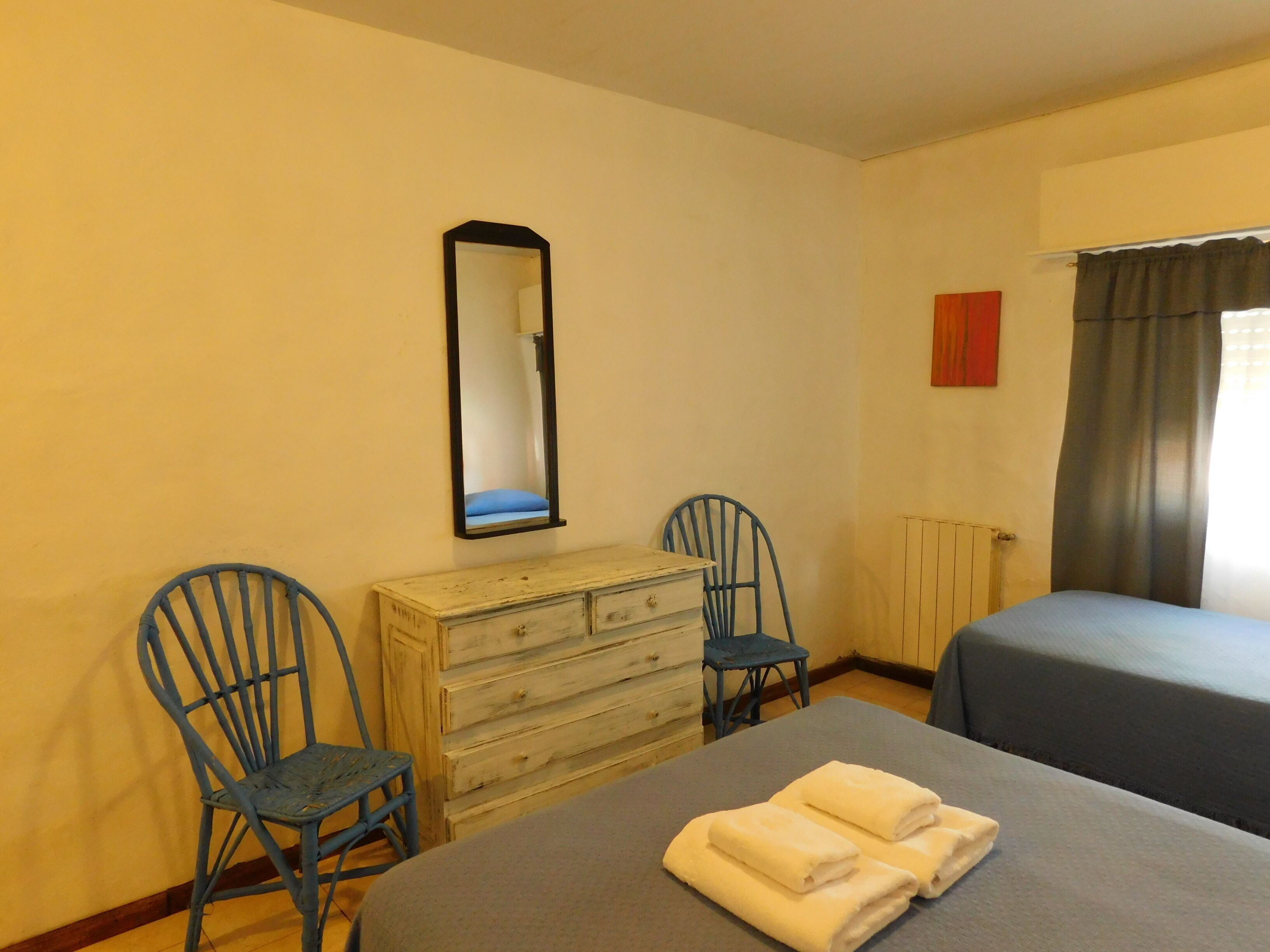 A room with two beds, a dresser, two chairs, a mirror, and a window with curtains.