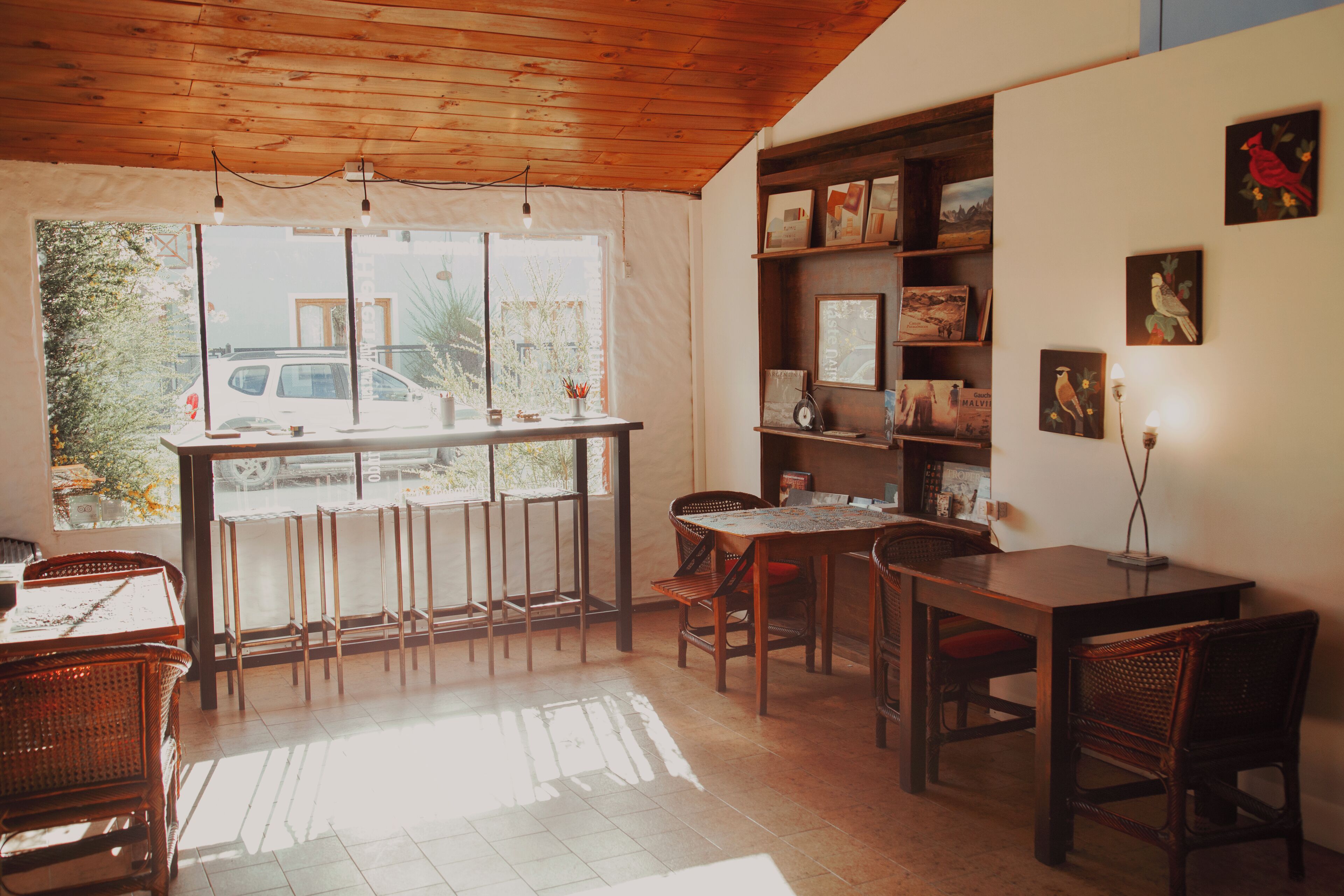 A dining area with a wooden ceiling, a large window, and a bookshelf with framed pictures.
