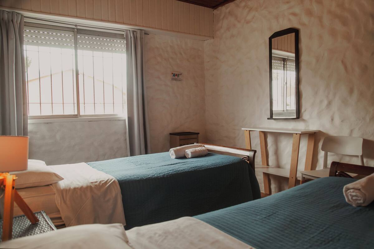 Une chambre d’hôtel avec deux lits, un bureau, une chaise, une petite table et une fenêtre avec des rideaux.