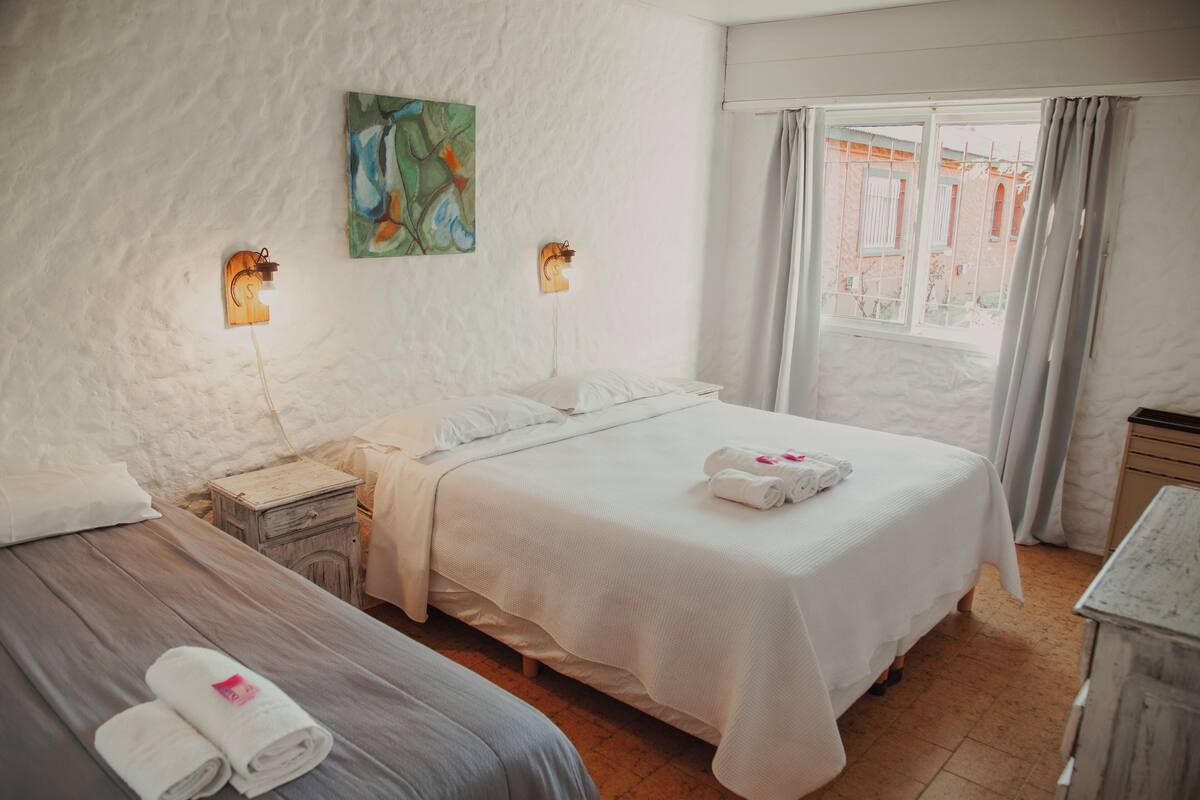 Une chambre d’hôtel avec deux lits, une table de chevet, un tableau au mur et une fenêtre avec des rideaux.