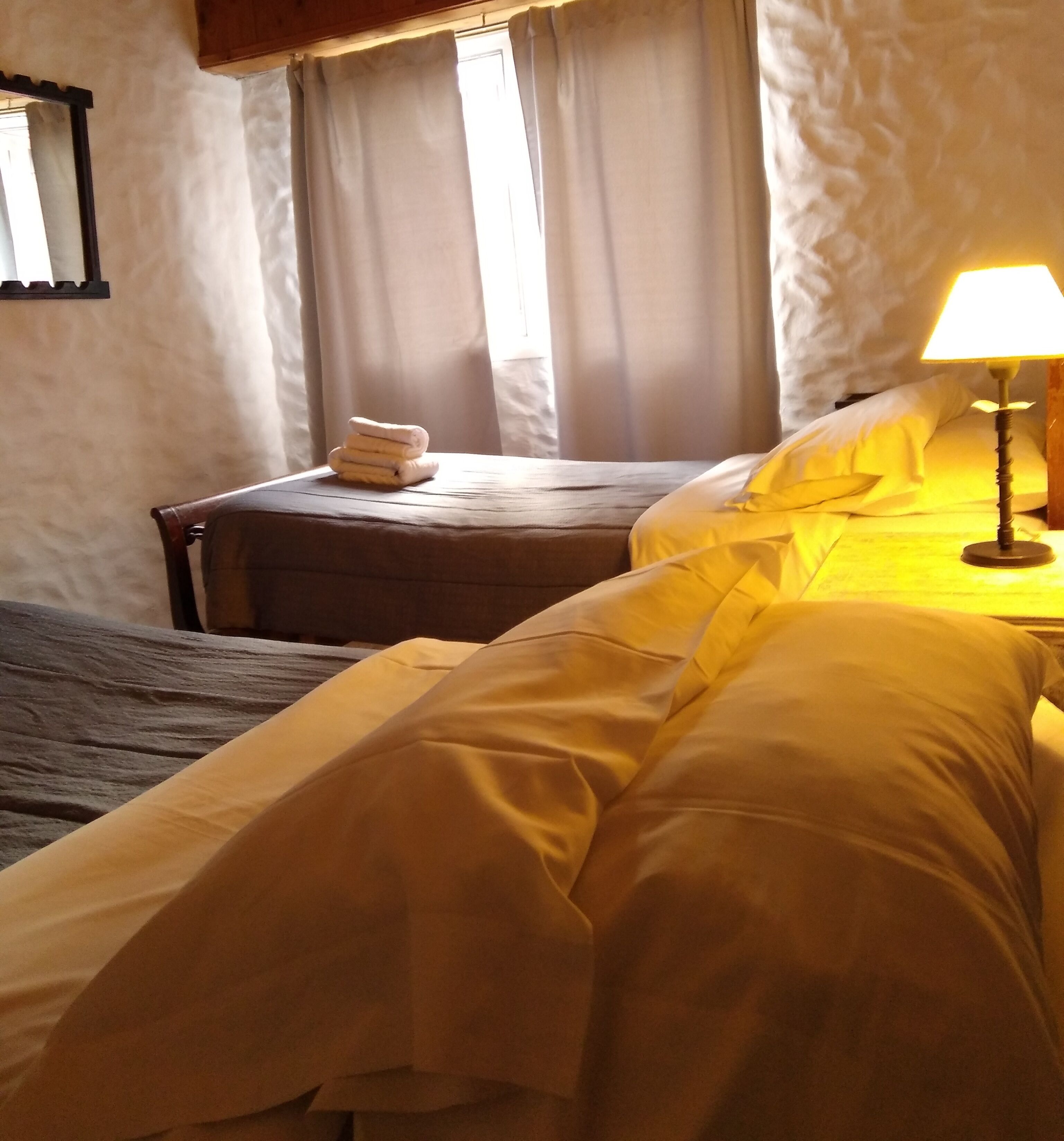 A hotel room with a bed, a bedside table, a lamp, and a window with curtains.