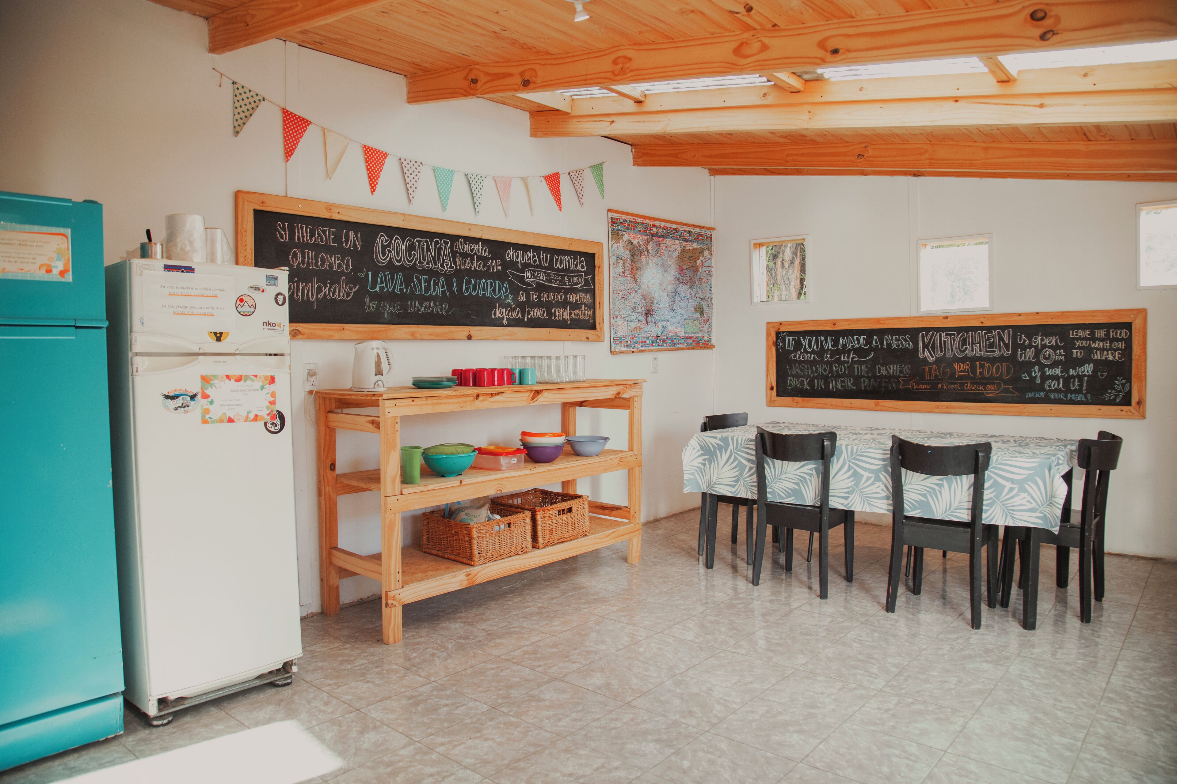 A kitchen with a chalkboard menu, wooden shelves, and a teal refrigerator.