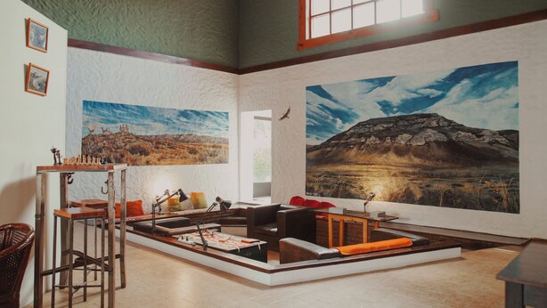 Une pièce spacieuse ornée d’un grand tableau représentant un paysage montagneux, d’un jeu d’échecs et d’un coin salon confortable avec une cheminée.