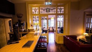 A bar area with a wooden counter, stools, and a red leather couch. - Heath Cottage Hotel (Dewsbury)