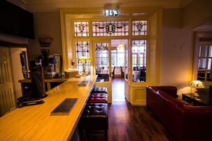 Uma área de bar com balcão de madeira, banquetas e um sofá de couro vermelho.