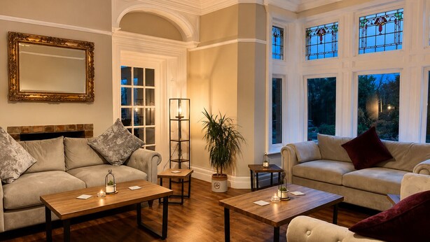 A well-lit living room with a sofa, armchair, coffee table, and a floor lamp. - Heath Cottage Hotel (Dewsbury)