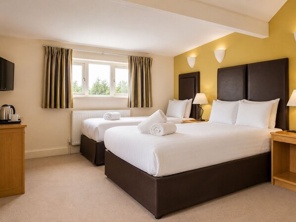 A hotel room with a large bed, two bedside tables, a TV, a window with curtains, and a radiator.