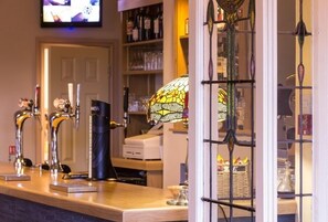 Uma área de bar com várias torneiras, uma máquina de café expresso preta e uma janela de vitral.