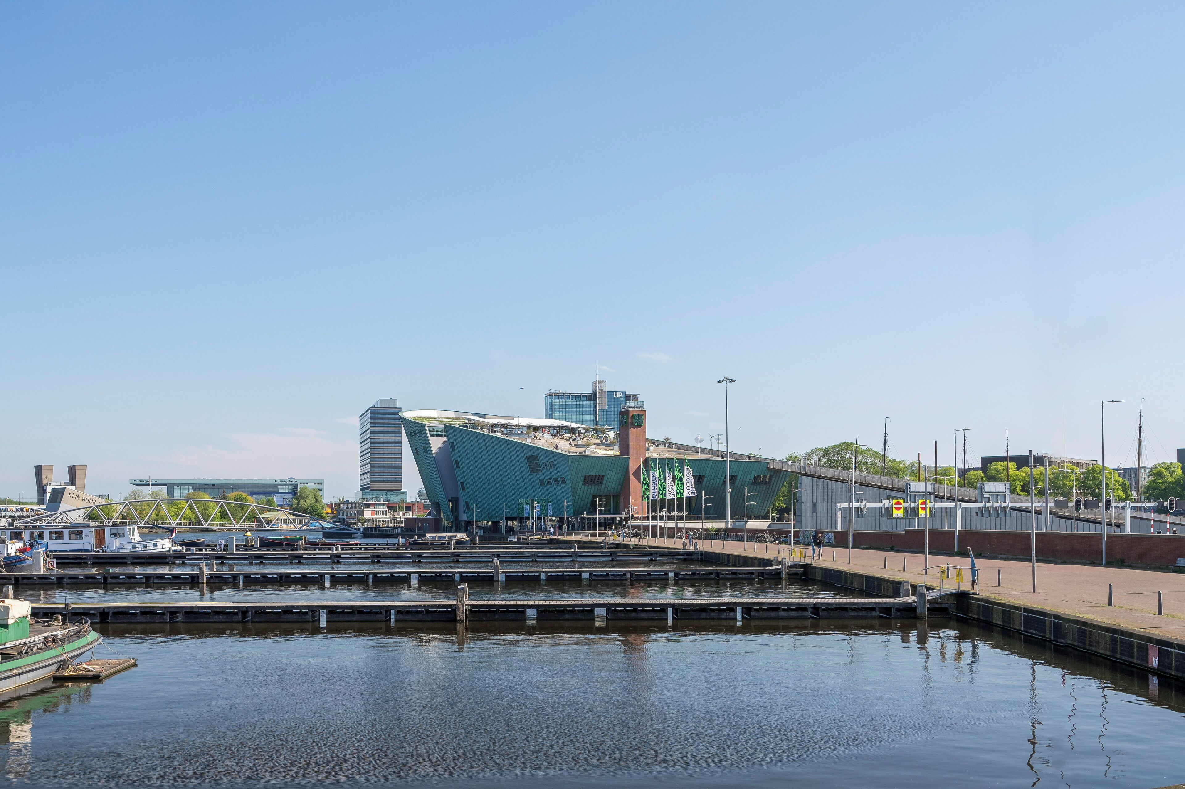 A waterfront area with a modern building, a bridge, and a marina.