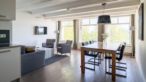 A modern kitchen with a built-in oven, a dining area with a wooden table and chairs, and a gray sofa. - Amsterdam Centre Harbour Apartments (Amsterdam)