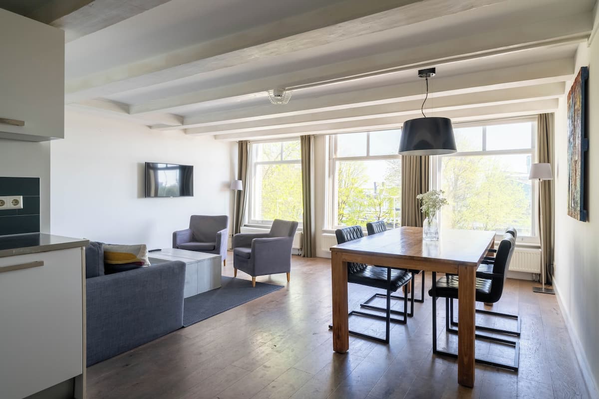 Une cuisine moderne dotée d’un four encastré, un coin repas avec une table et des chaises en bois, et un canapé gris.