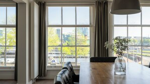 A dining area with a large window, a wooden table, and a vase with flowers. - Amsterdam Centre Harbour Apartments (Amsterdam)