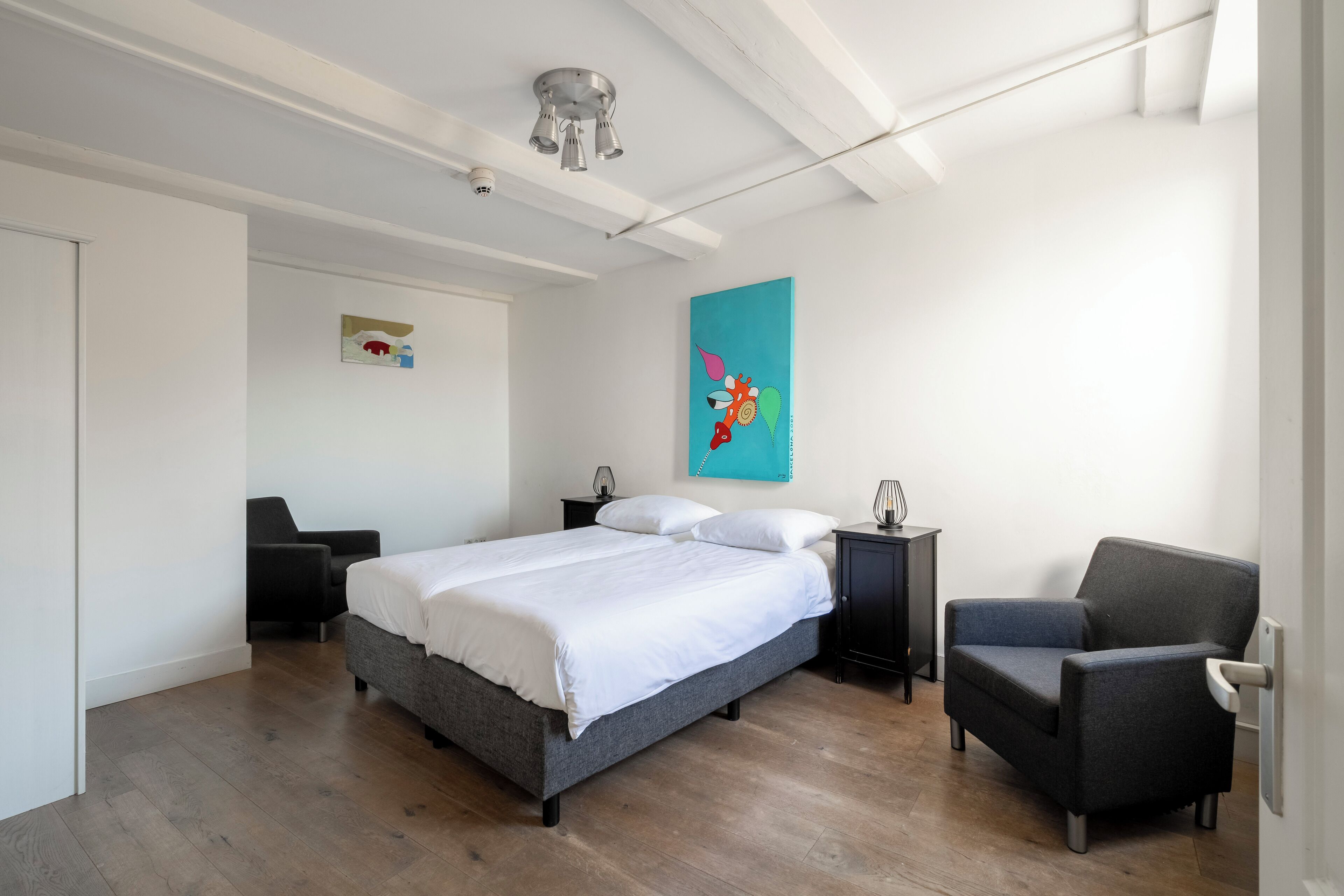 Une chambre à coucher moderne avec un grand lit, une chaise, une table de chevet et un tableau accroché au mur.