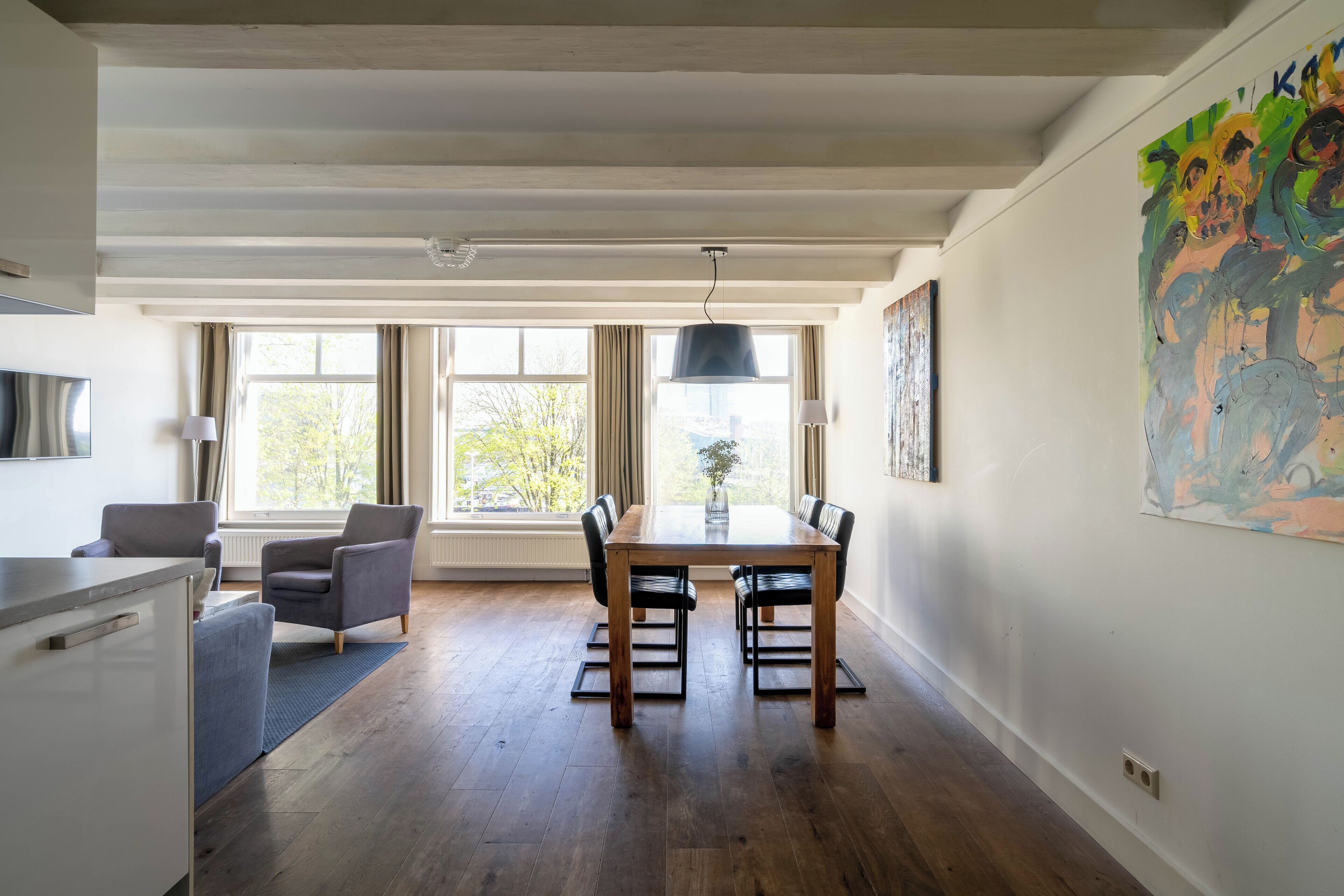 A dining area with a wooden table and chairs, a kitchen area with a counter and cabinets, and a large window with curtains.