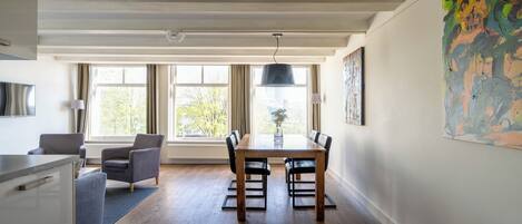 A dining area with a wooden table and chairs, a kitchen area with a counter and cabinets, and a large window with curtains.