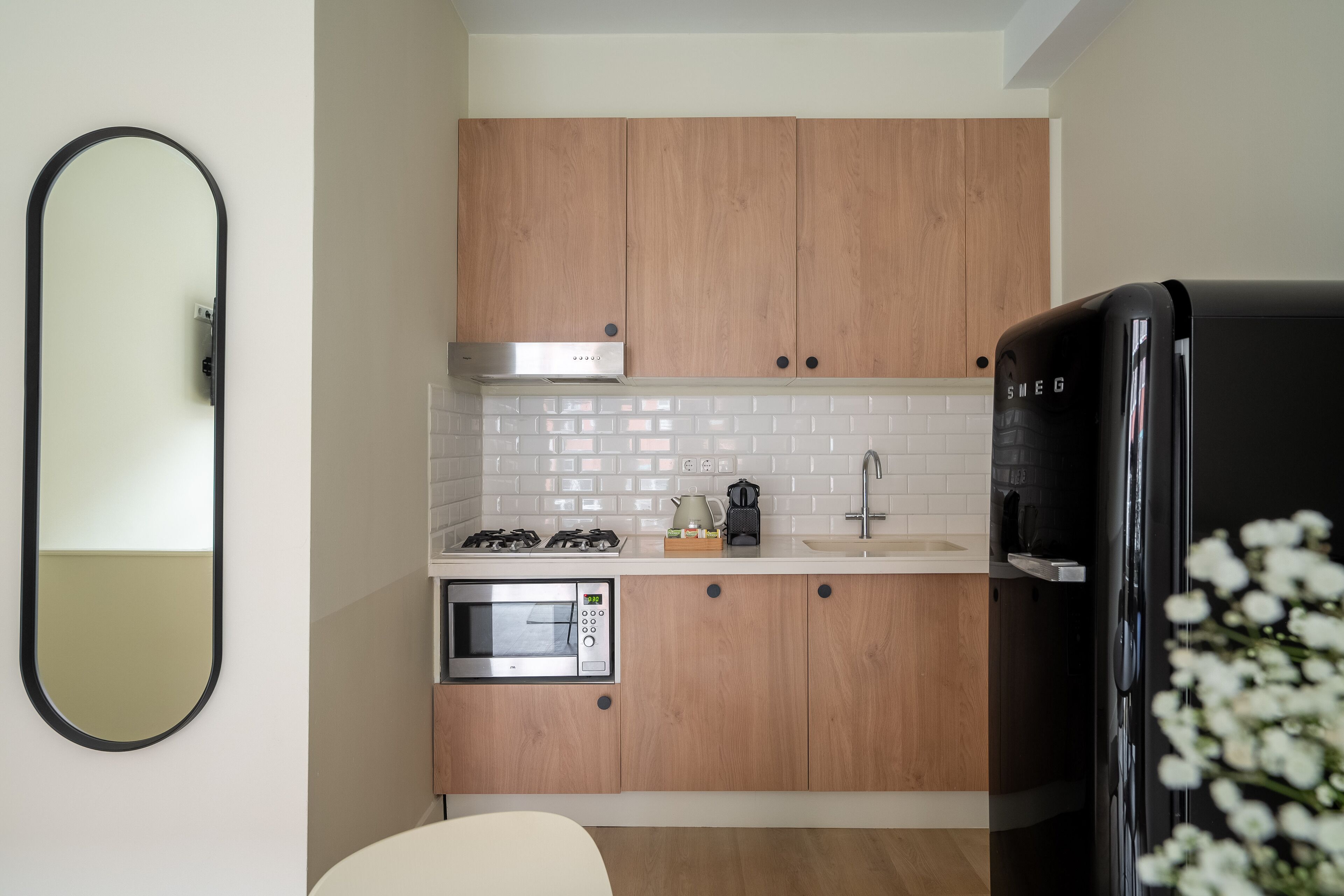 Una cocina compacta con armarios de madera, un refrigerador negro, un microondas y una estufa a gas.