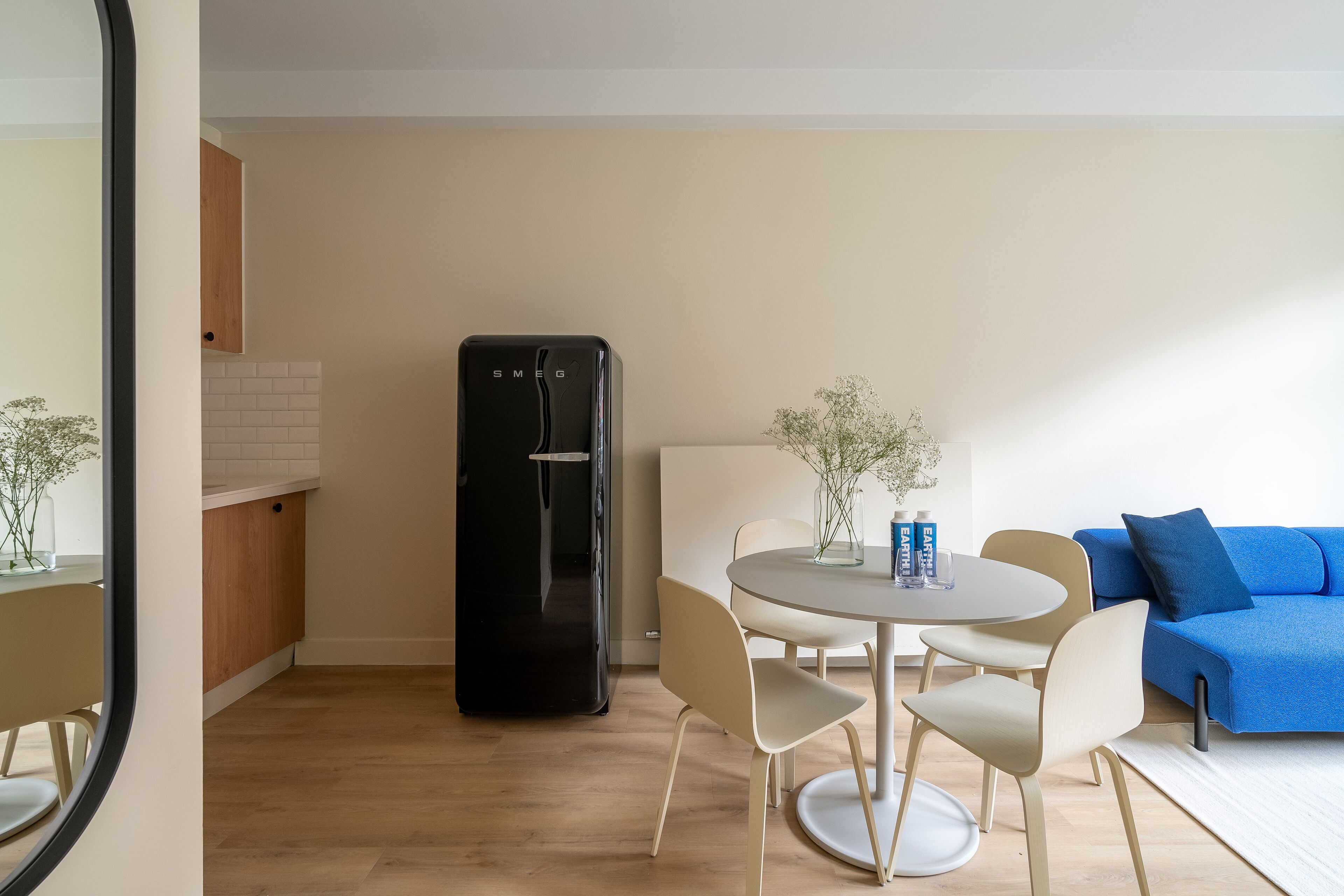 A modern living room with a black refrigerator, a round dining table with chairs, and a blue sofa.