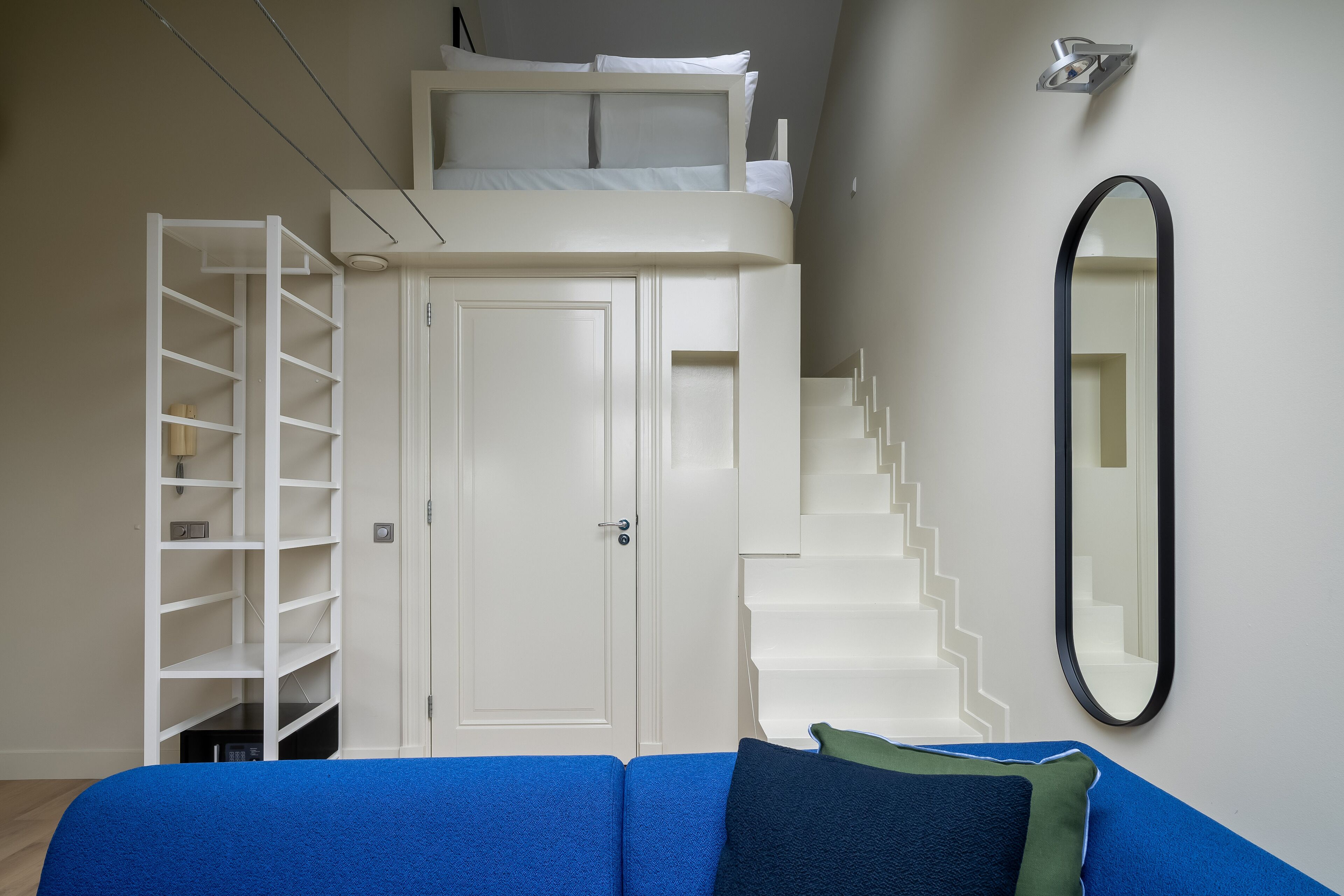 Una habitación pequeña con una litera, un armario blanco, un sofá azul y un espejo en la pared.