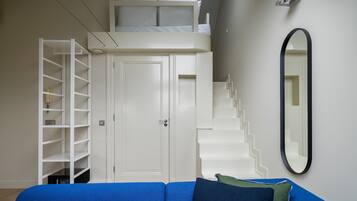 Una habitación pequeña con una litera, un armario blanco, un sofá azul y un espejo en la pared.