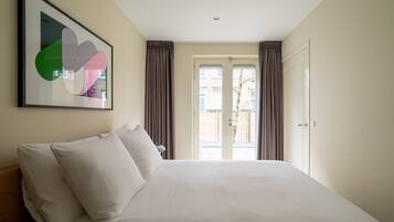 A hotel room with a large bed, a framed abstract artwork, and a view through a glass door.