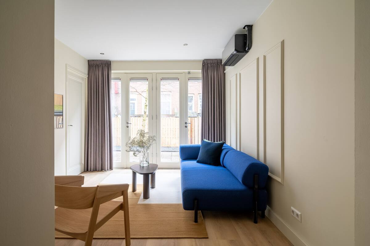 A modern living room with a blue sofa, wooden furniture, and a view through glass doors.