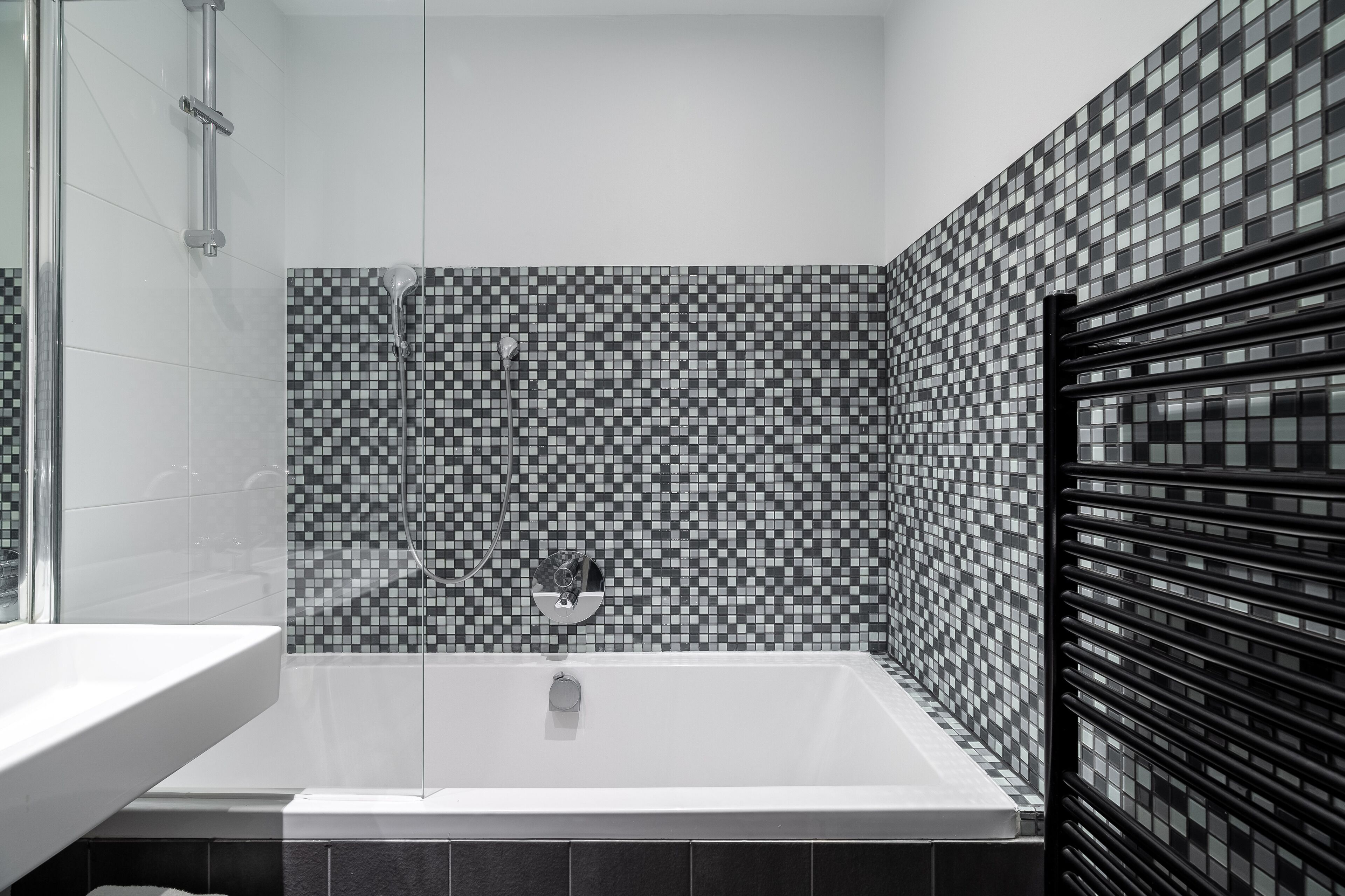 Een moderne badkamer met een groot bad, een douchegedeelte en een betegelde muur met een ruitpatroon.