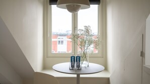 Een kamer met een ronde tafel, twee flessen met de aanduiding 'EARTH', een bloemenvaas en een groot raam met uitzicht op gebouwen.
