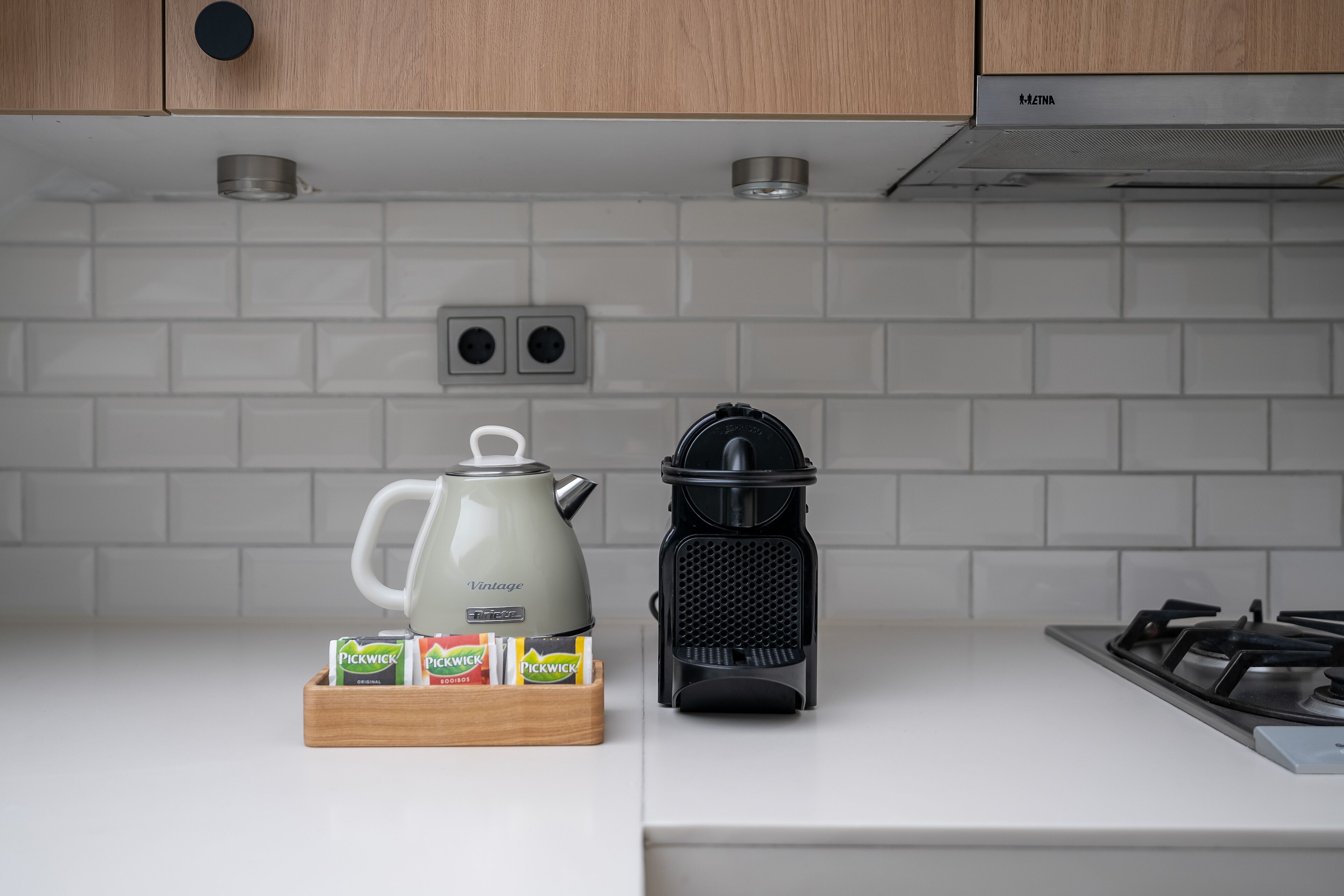 A kitchen with a white countertop, a kettle, a coffee maker, and a box of Pickwick tea bags.