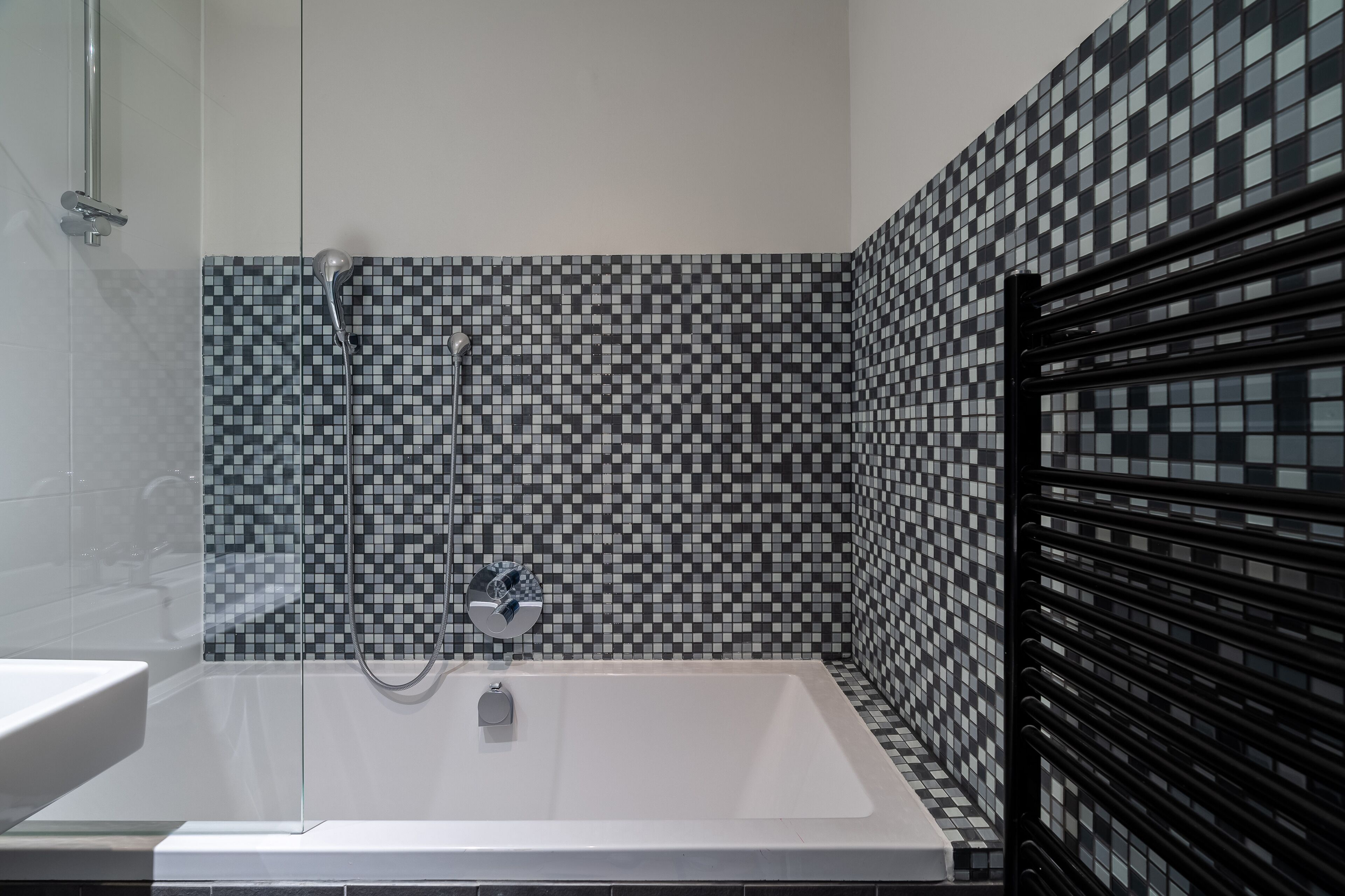 Un baño moderno con salpicadero de azulejos a cuadros, una bañera blanca y un perchero negro.