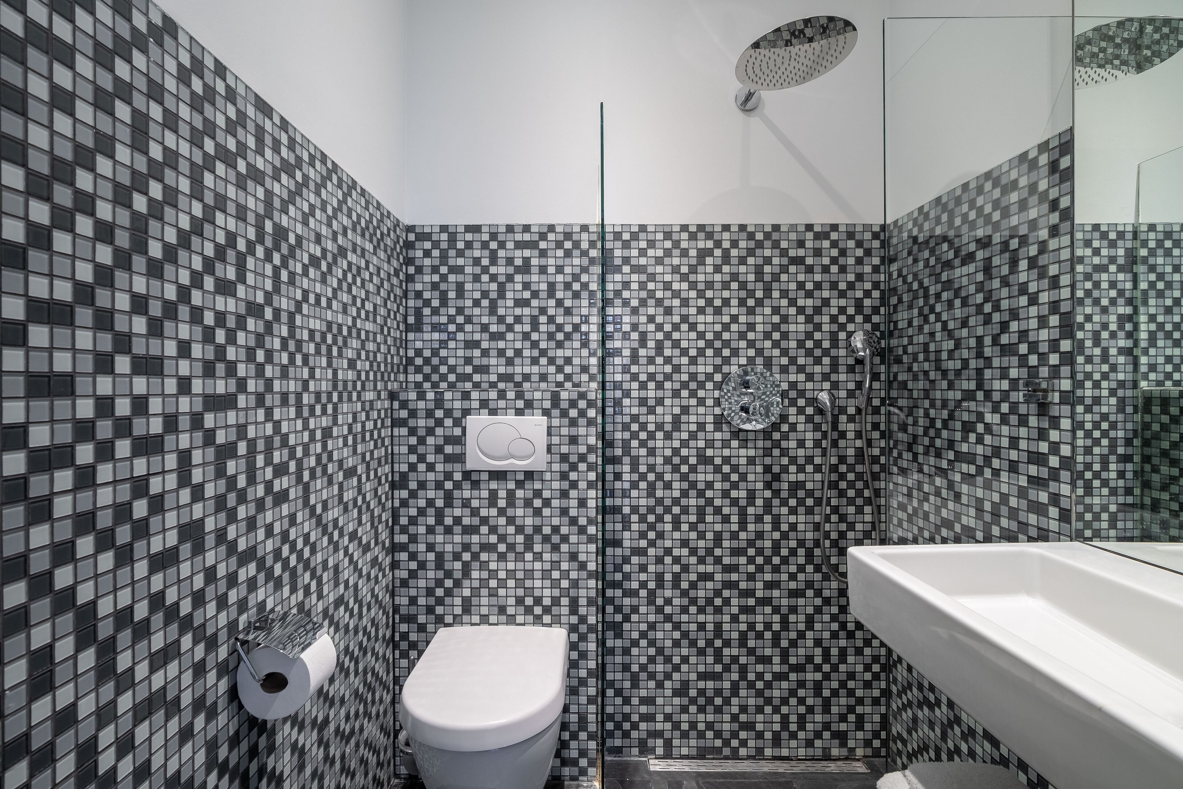 A bathroom with a checkered tile pattern, a toilet, a shower, and a sink.