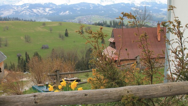 Un paysage rural avec une clôture en bois, un bâtiment à toit rouge et, au loin, une vue sur des montagnes enneigées.
