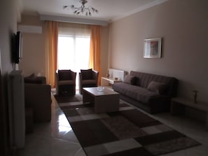 Ein Wohnzimmer mit einer Couch, zwei Sesseln, einem Couchtisch und einem Fernseher auf einem Schrank.