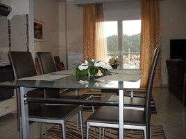 Comedor con mesa de vidrio, sillas de metal y vistas a un paisaje montañoso a través de amplios ventanales.