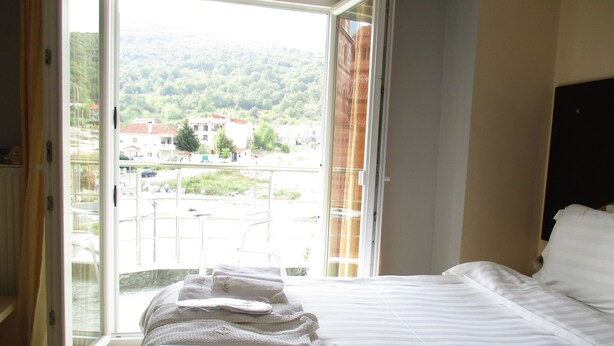 Ein Hotelzimmer mit einem Bett, einem Fenster mit Blick auf eine Stadt und Hügel sowie einer Reihe Handtüchern auf dem Boden.