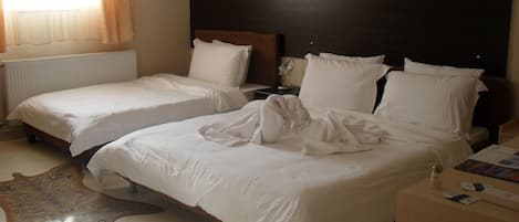 Habitación de hotel con dos camas, un cabecero de madera, una alfombra blanca y una mesita de noche con una lámpara.
