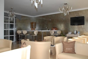 Un salón moderno con sofás beige, una araña y un televisor de pantalla plana montado en una pared texturizada.