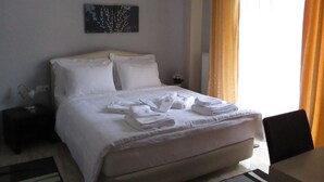 Ein ordentlich bezogenes Bett mit weißen Leinen und Handtüchern, ein kleiner Nachttisch mit Lampe und ein Bild an der Wand.