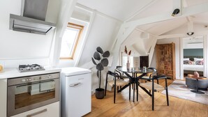 A modern kitchen with a built-in oven, a compact refrigerator, and a dining area with a wooden table and chairs. -  Numa Amsterdam Helmers (Amsterdam)