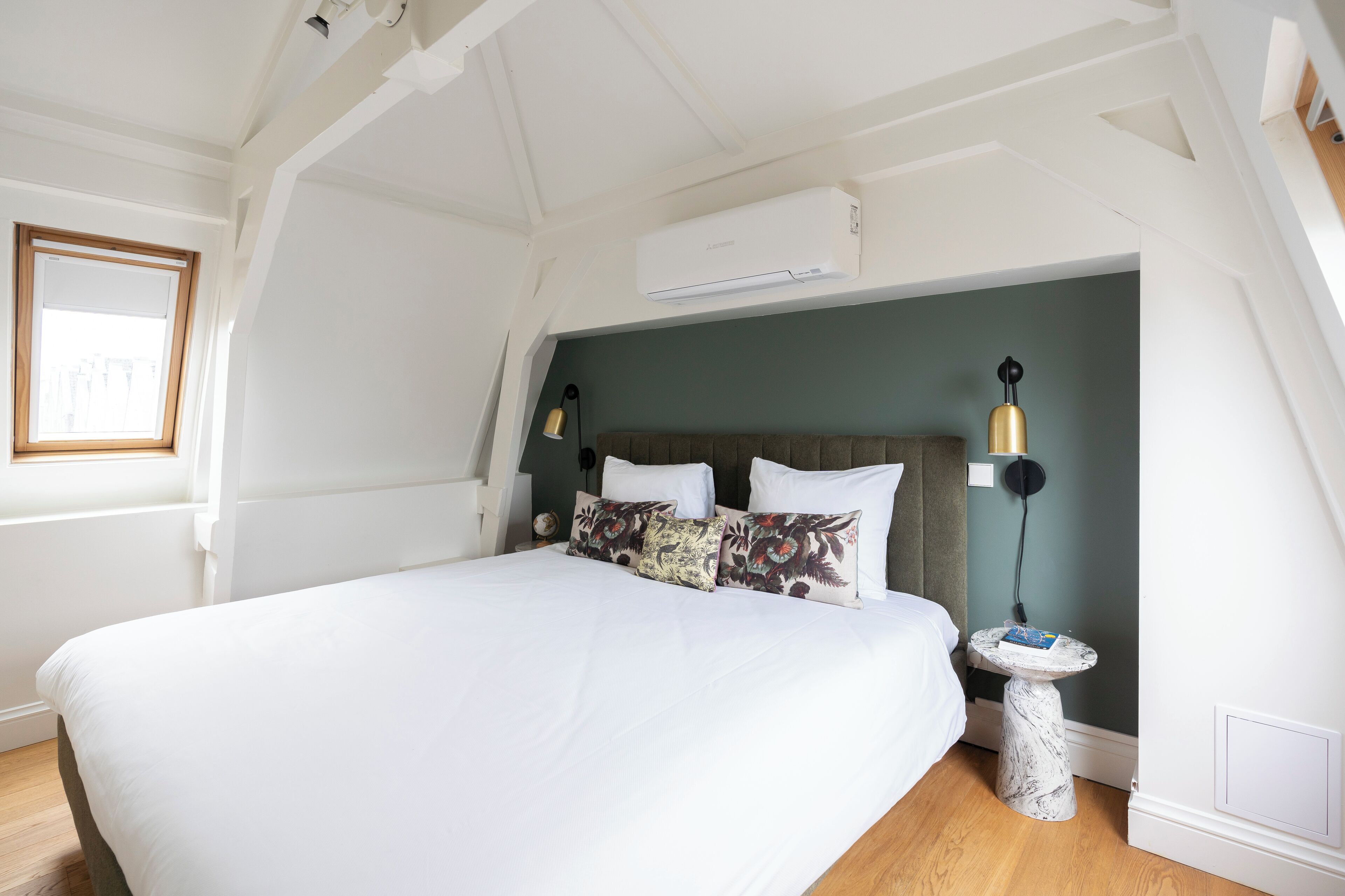 Une chambre à coucher avec un grand lit, une tête de lit, une table de chevet et une fenêtre.