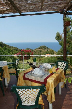 An outdoor dining area with tables set for two, overlooking a scenic view of the sea and hills. - Hôtel Sant'Andrea, The Originals Relais (Relais du Silence) (Marciana)
