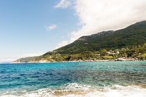 A coastal landscape with a clear view of the sea, a mountain with dense vegetation, and a few buildings on the hillside. - Hôtel Sant'Andrea, The Originals Relais (Relais du Silence) (Marciana)