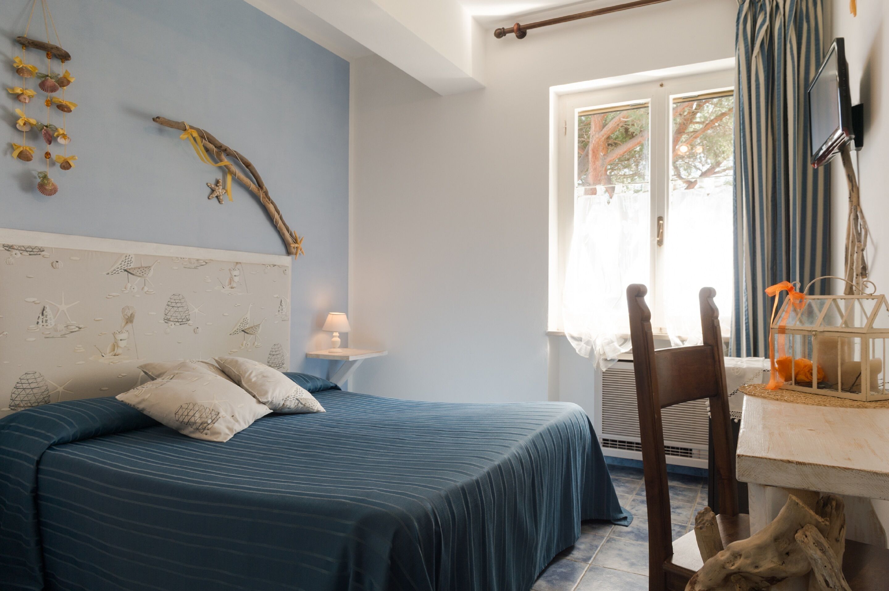 A bedroom with a bed, a nightstand, a lamp, a window with curtains, and a TV mounted on the wall.