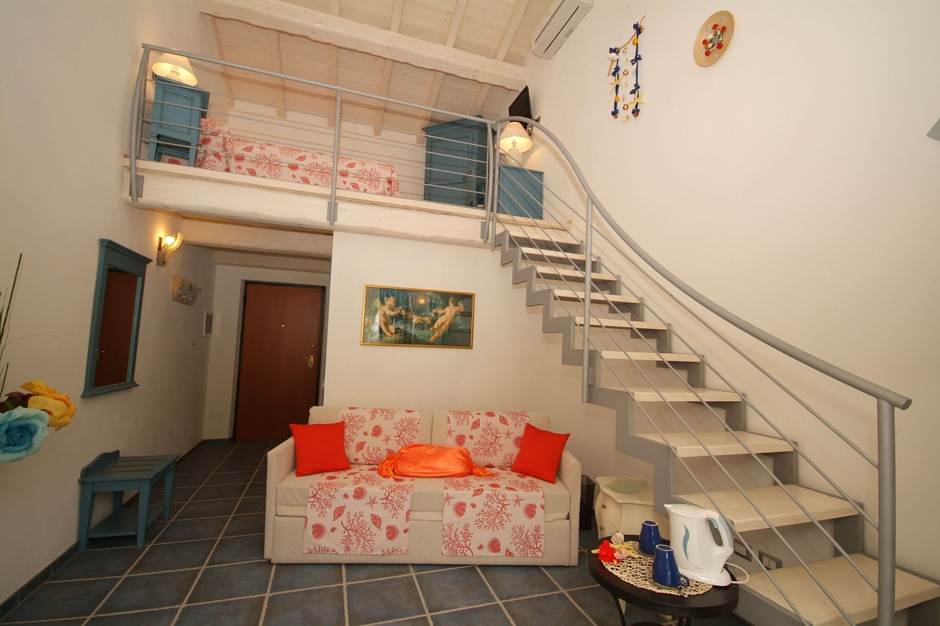 A two-story apartment with a staircase, a sofa with red cushions, a painting, and a coffee table with cups and a kettle.