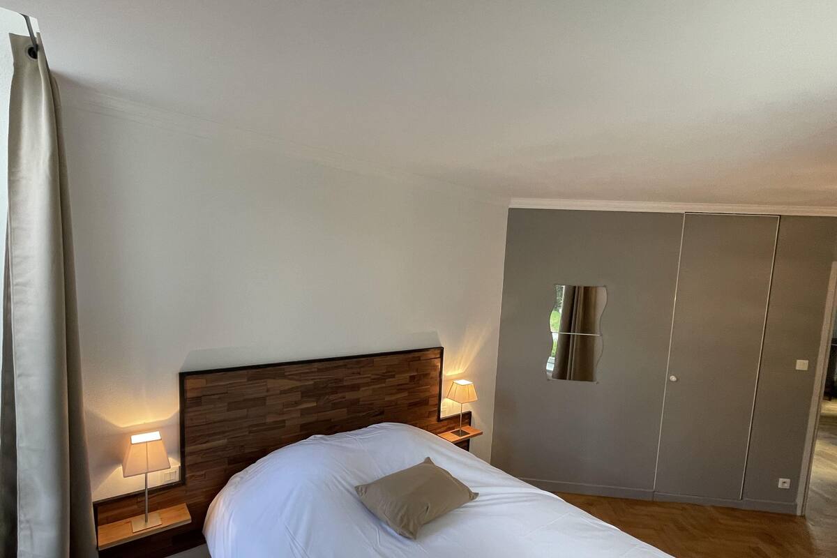 A bedroom with a bed, nightstands, a lamp, a wardrobe, and a mirror.
