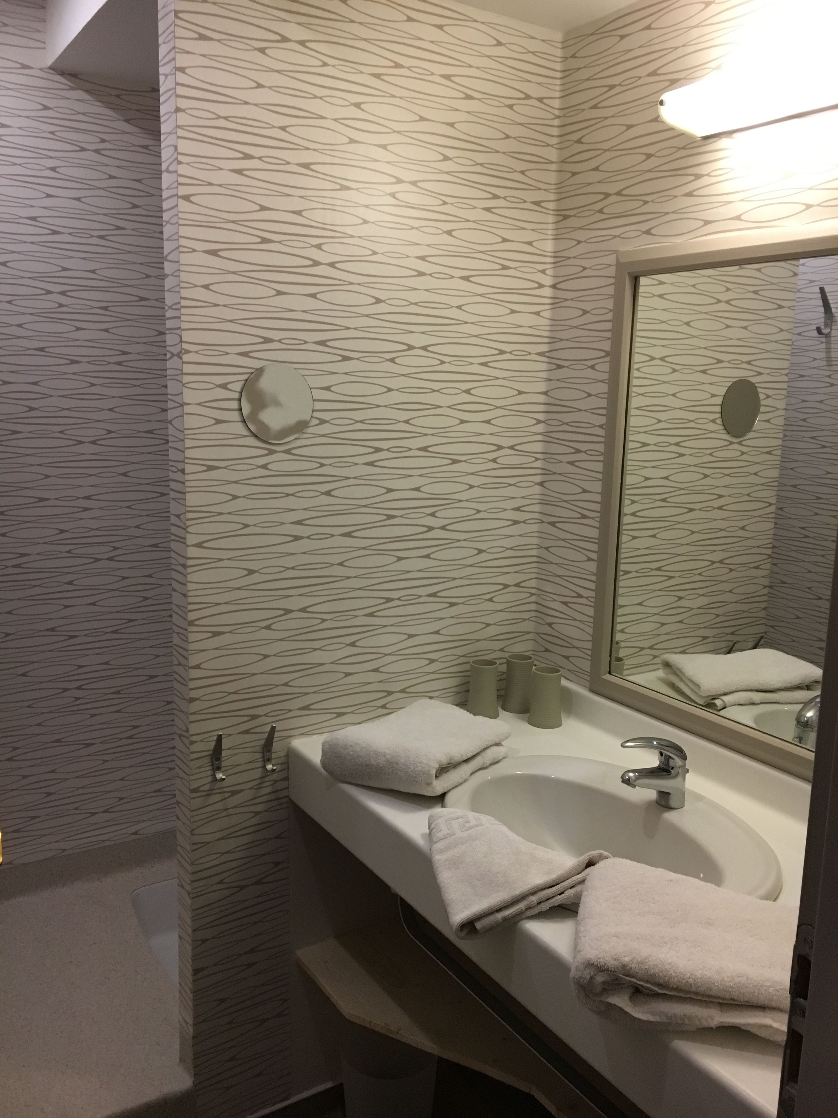 A bathroom with a patterned wall, a sink with a mirror, and two towels on the counter.