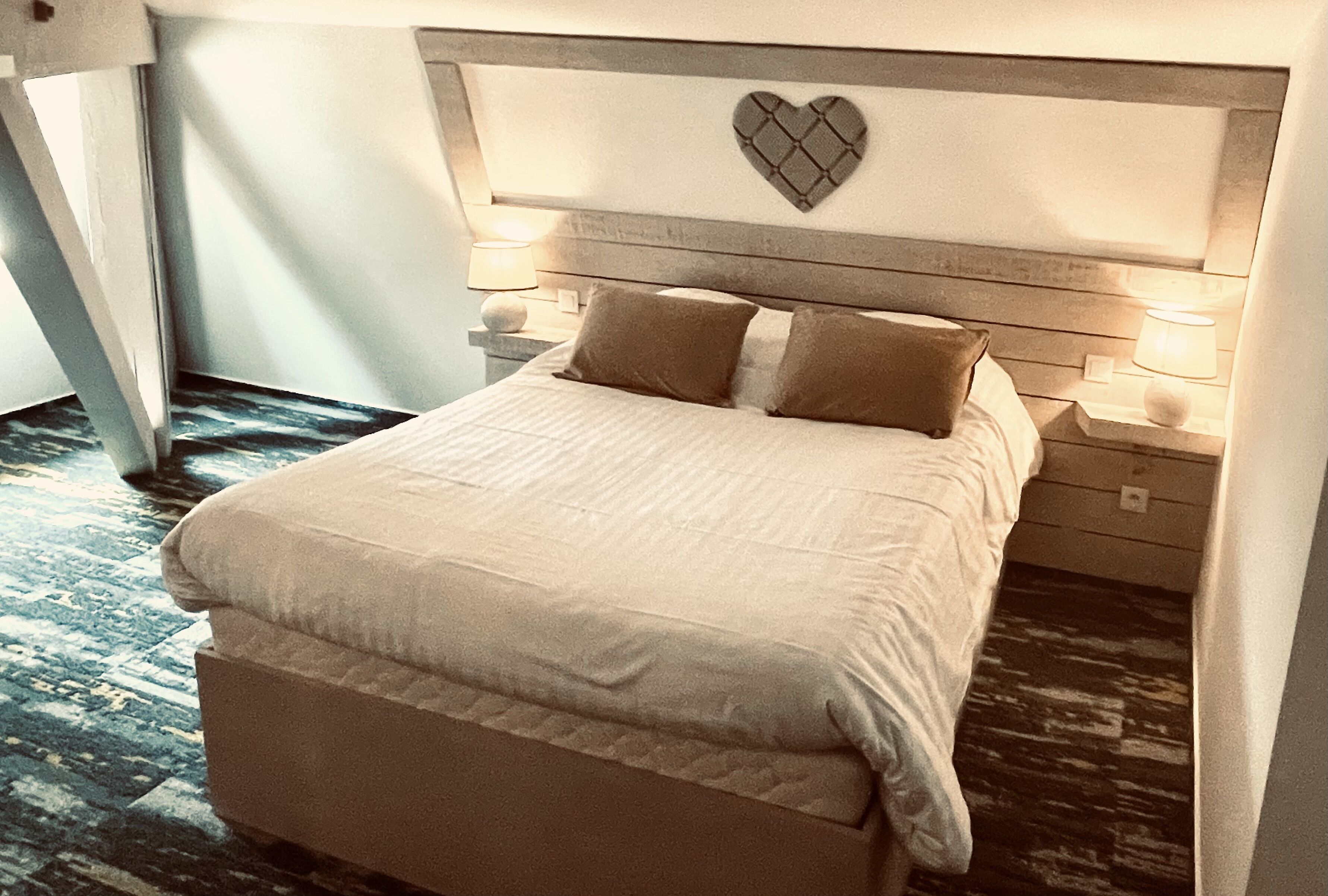 A neatly made bed with a heart-shaped headboard, two bedside lamps, and a wooden nightstand.
