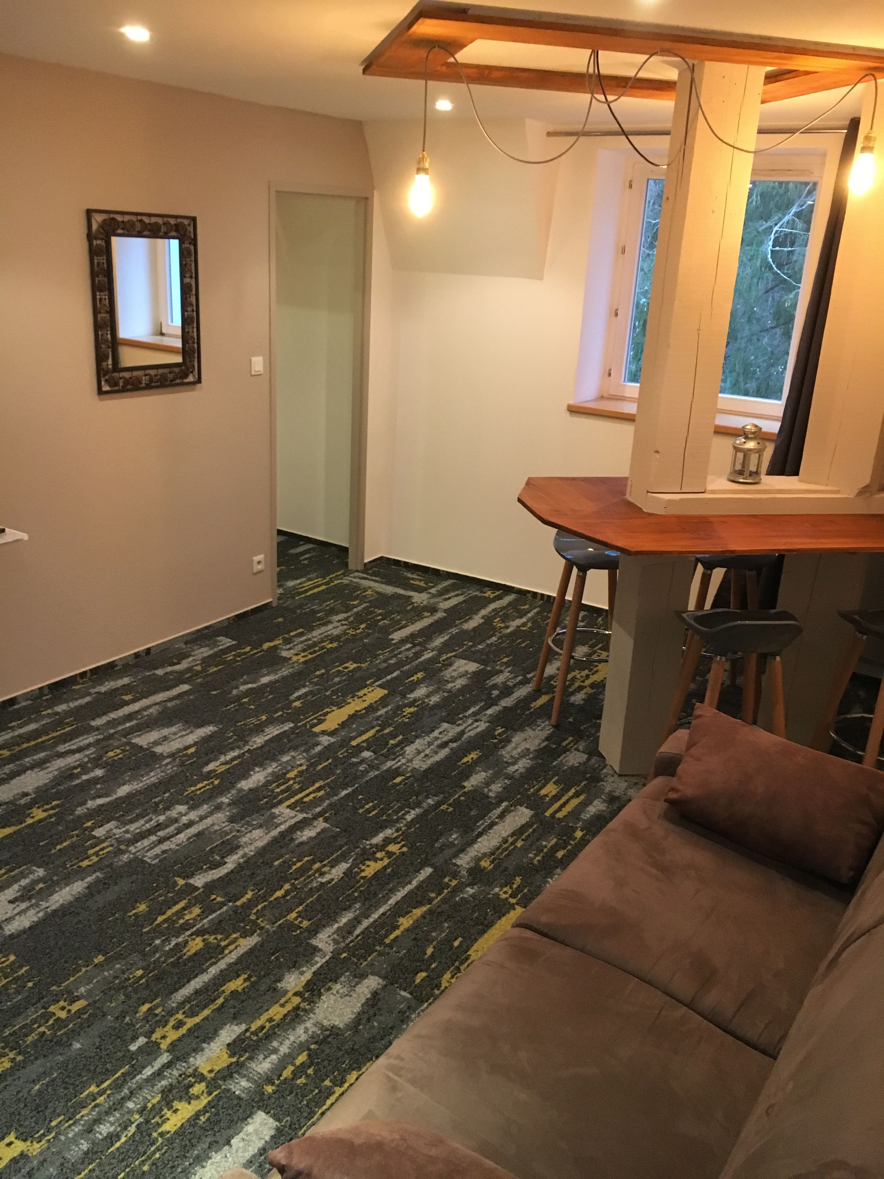 Um quarto com carpete estampado, um sofá marrom, uma mesa de madeira com cadeiras e um espelho na parede.